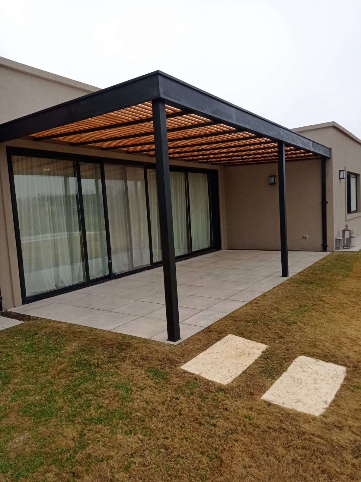 Pérgola metálica sobre patio con piso de porcelanato